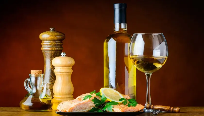Un plat de saumon avec citron et persil, accompagné d'une bouteille et d'un verre de bon vin blanc sec, d'une salière, d'une poivrière et d'une burette d'huile d'olive.
