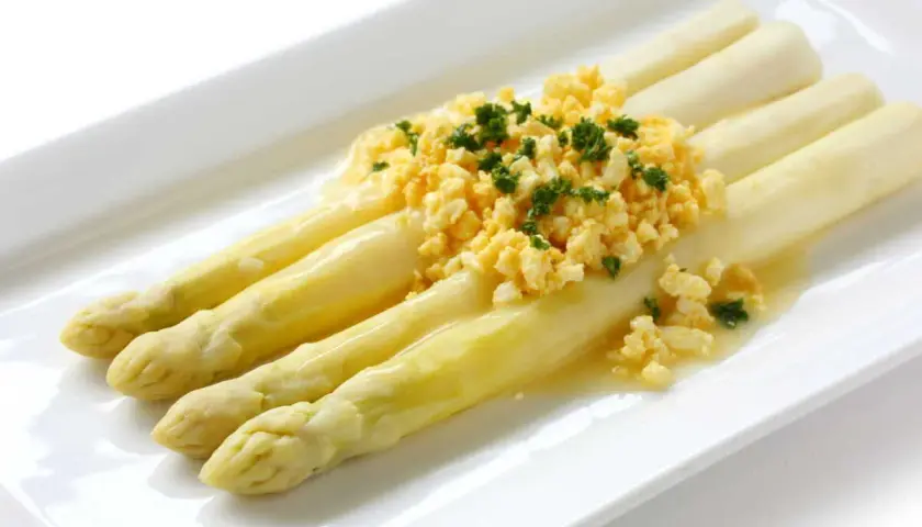 Asperges à la flamande : des asperges blanches tendres nappées d'une sauce savoureuse et garnies d'œufs brouillés et de persil frais.