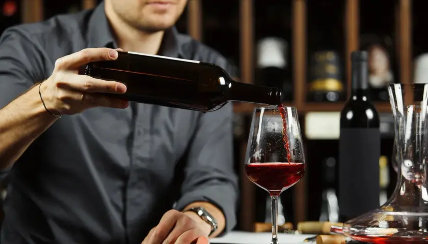 Un homme verse un vin rouge profond dans un verre, une cave à vin en arrière-plan. Quel vin rouge savoureux !