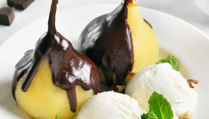 Poires pochées nappées de chocolat noir, servies avec de la glace à la vanille et des éclats de noisettes. Un délice de poire Belle Hélène.