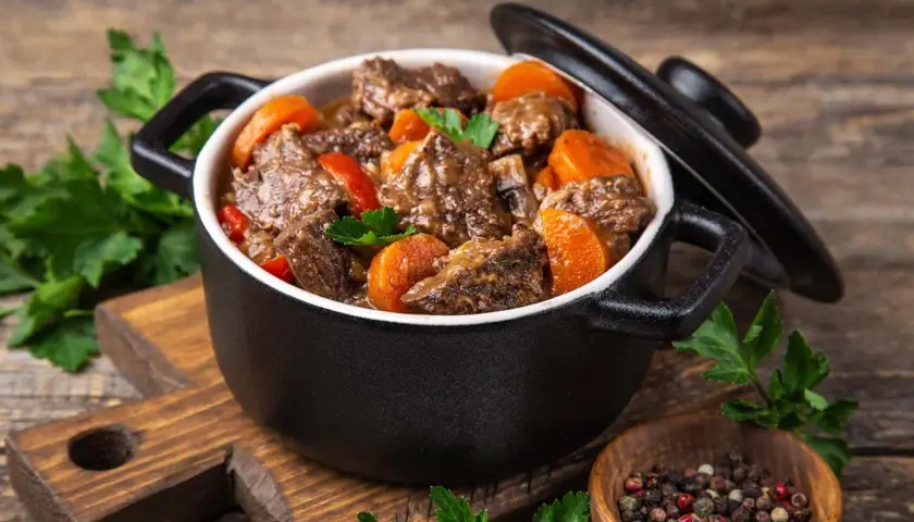 Un délicieux bœuf bourguignon mijoté dans une cocotte minute SEB, garni de carottes et de persil frais. Un plat réconfortant prêt à être dégusté.