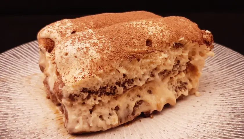Un généreux tiramisu au café, saupoudré de cacao, repose sur une assiette striée.