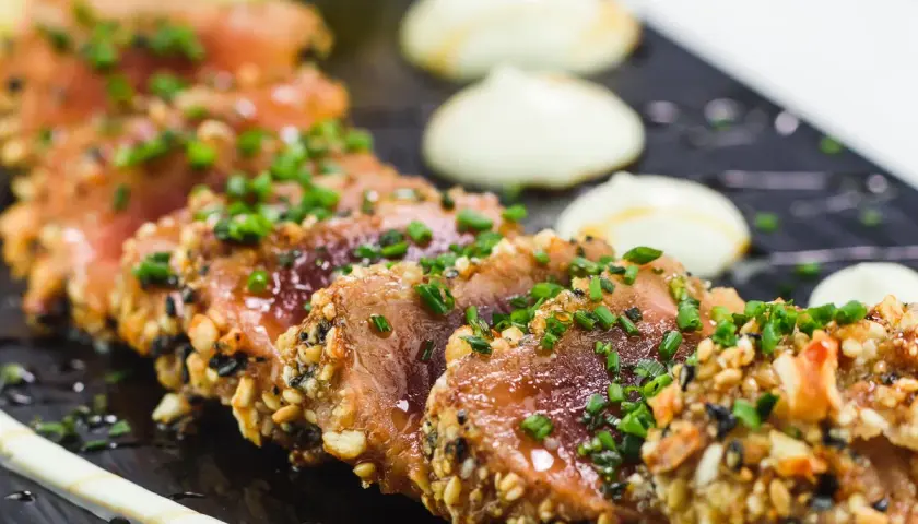 Tataki de thon en croûte de sésame et noix, garni de ciboule fraîche. Un accompagnement visuellement appétissant.