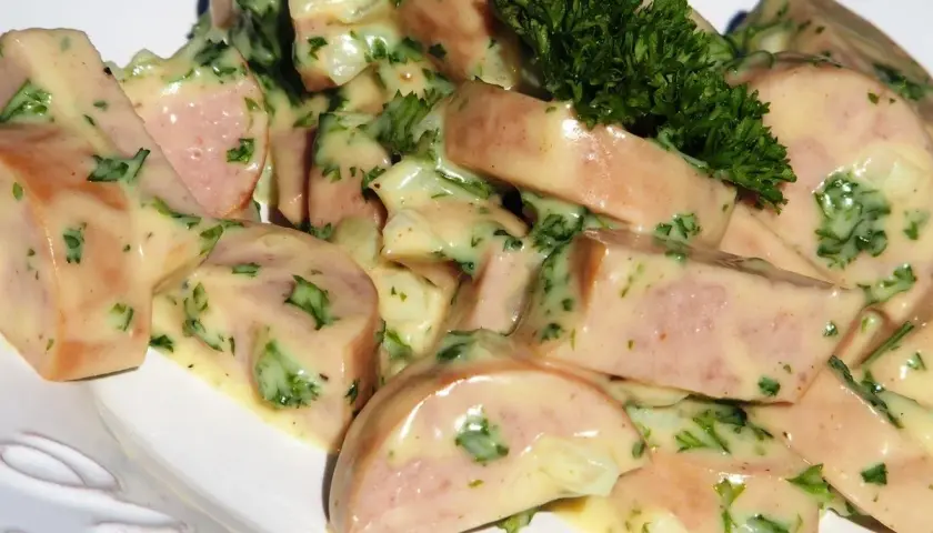 Une délicieuse salade de cervelas, coupée en dés et nappée d'une sauce crémeuse aux herbes fraîches, garnie d'une touche de persil.