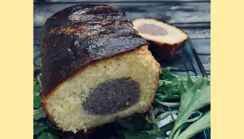 Un délicieux saucisson brioché, coupé en deux, repose sur un lit de verdure. Sa croûte dorée et sa mie moelleuse invitent à la dégustation.