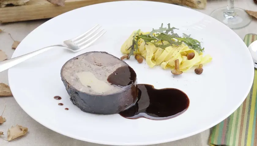 Un rôti de lièvre à la royale, garni de foie gras, servi avec des pâtes fraîches, des champignons et une sauce au vin.
