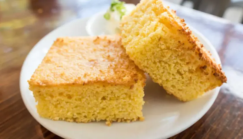 Deux parts de pain au maïs dorées et moelleuses sur une assiette blanche, avec une petite portion de beurre et de ciboule en arrière-plan.