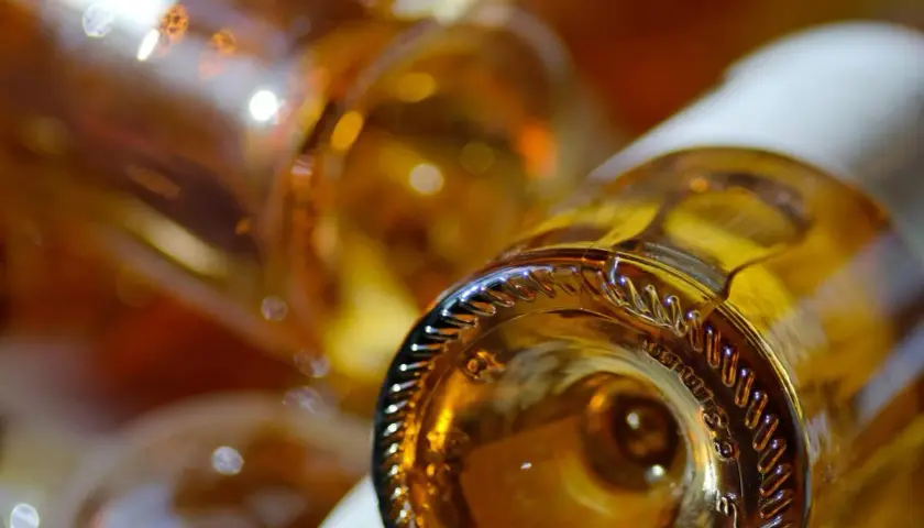 Gros plan sur le goulot d'une bouteille de vin ambré, évoquant un sauterne sec ou moelleux. Reflets lumineux sur le verre.