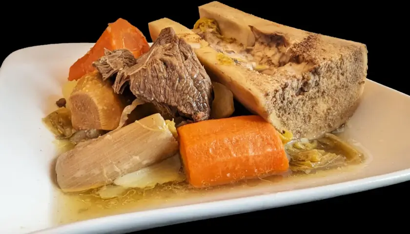 Un plat généreux de pot-au-feu cocotte minute : viande, os à moelle, carottes et poireaux mijotés dans un bouillon savoureux.