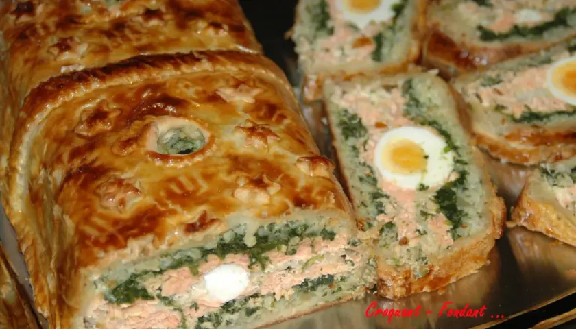 Un koulibiac de saumon doré, garni d'épinards et d'œufs durs, est coupé en tranches appétissantes.