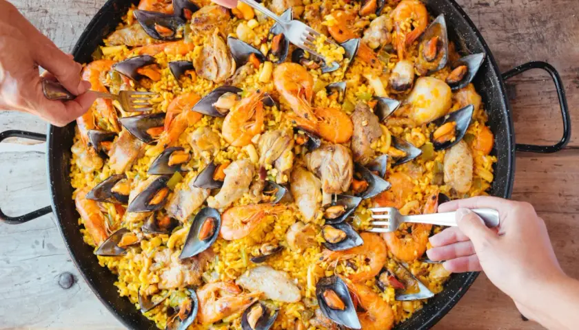 Un plat généreux de riz façon paella, garni de crevettes, moules et morceaux de poulet, prêt à être dégusté.