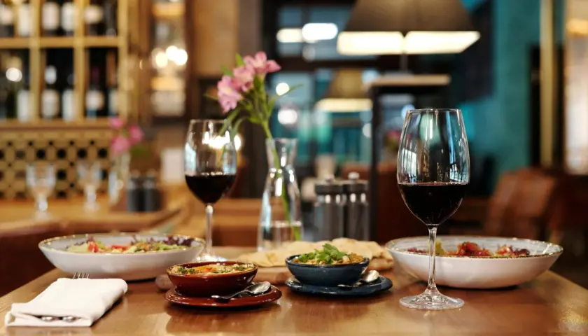 Verre de vin rouge tannique et puissant, accompagné de plats appétissants et d'une touche florale, dans une ambiance de restaurant chaleureuse.