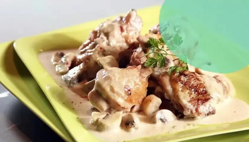 Un plat de fricassée de volaille crémeuse avec des champignons, garni de persil frais, servi dans une assiette jaune vif.