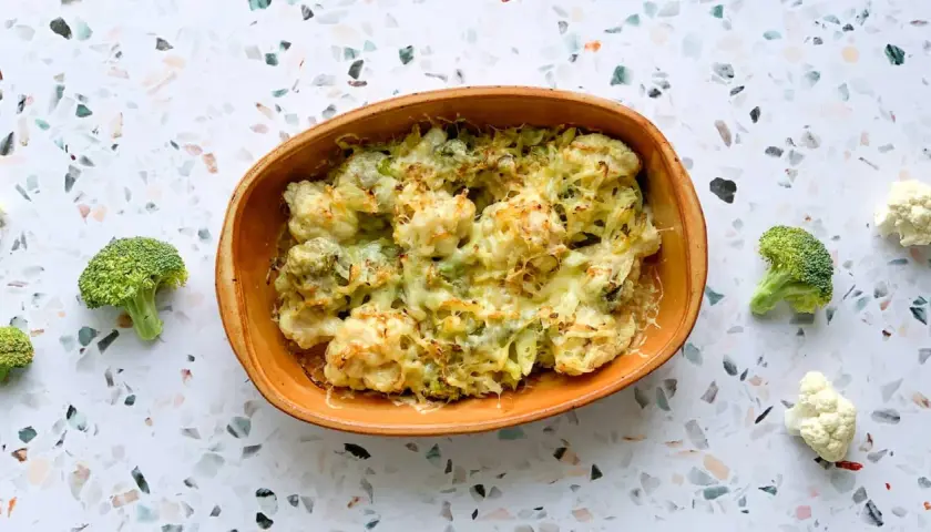Un délicieux gratin chou-fleur brocolis, gratiné au fromage, servi dans un plat en terre cuite. Quelques fleurons frais entourent le plat.