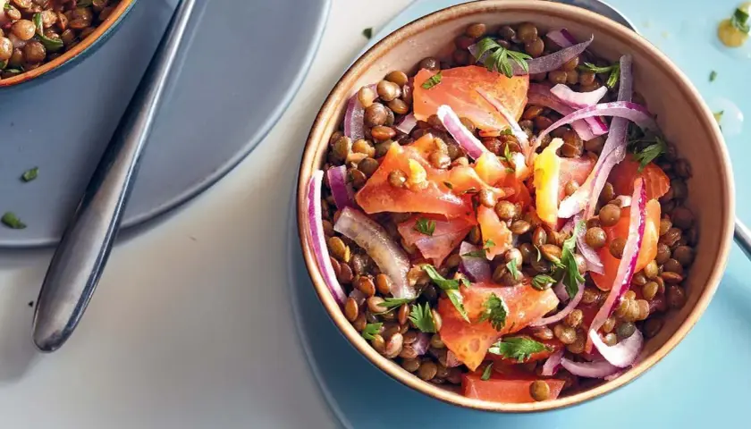 Salade de lentilles savoureuse avec du saumon fumé, des tomates et des oignons rouges, garnie de persil frais.