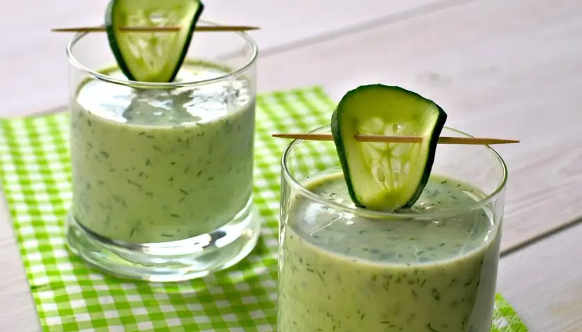Deux verres de gaspacho concombre, décorés d'une tranche de concombre sur un cure-dent, sur une nappe à carreaux verts.