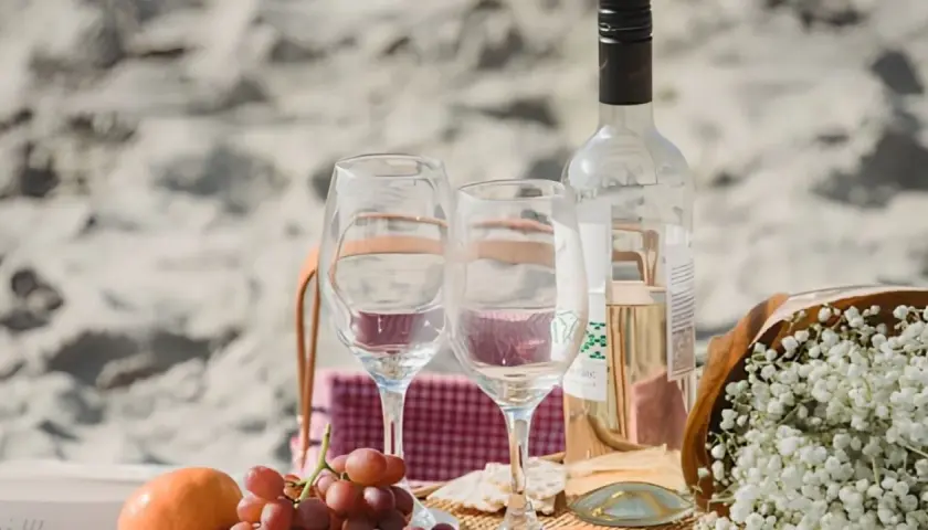Un pique-nique sur la plage avec des verres, des raisins et une bouteille de vin. Idéal pour savoir comment choisir un vin rosé parfait pour l'occasion.
