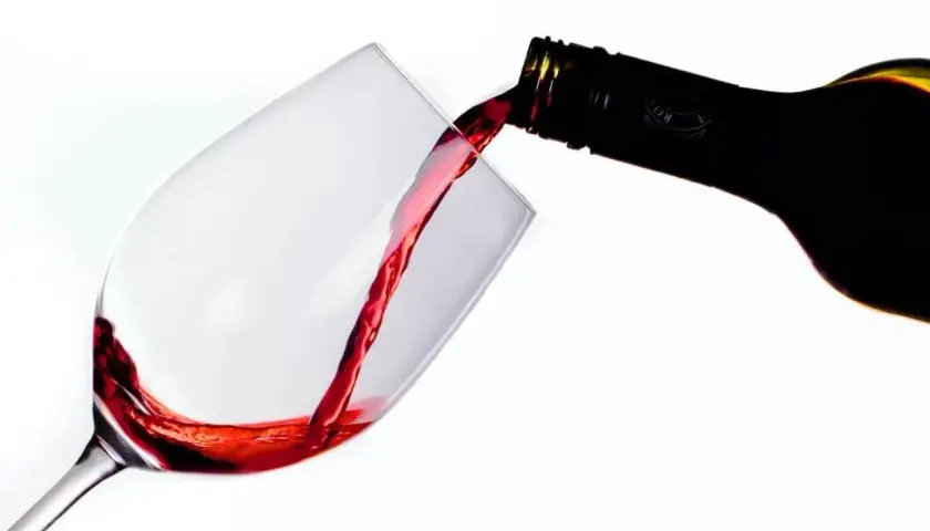 Le vin rouge, fruit d'une macération soignée, coule d'une bouteille dans un verre.