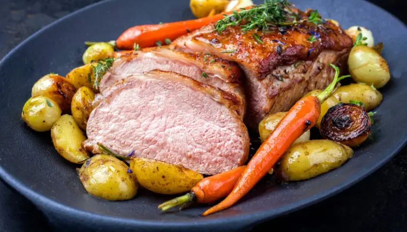 Délicieuse côte de veau barbecue, tranchée et servie avec des pommes de terre rôties et des carottes glacées, garnie d'herbes fraîches.