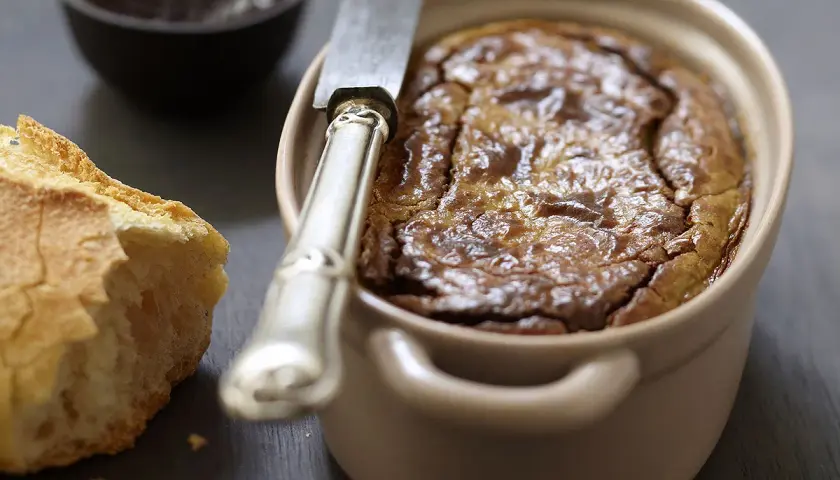 Un délicieux gâteau de foie de volaille à l'ancienne, servi avec du pain croustillant et une petite coupelle de confiture.