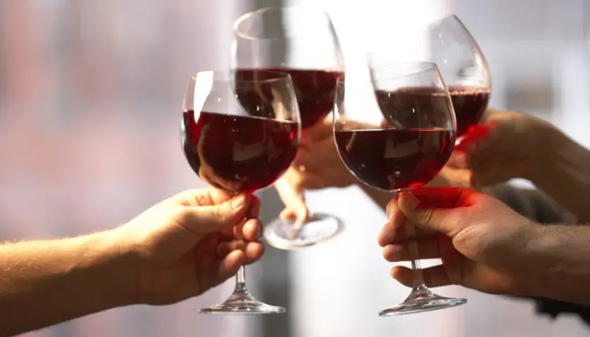Quatre mains portent des verres de vin rouge pour un toast. Une belle façon de célébrer et de savoir comment boire du vin rouge.