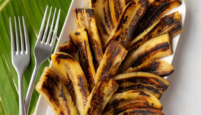 Bananes flambées grillées sur une feuille de bananier, prêtes à être dégustées avec deux fourchettes.