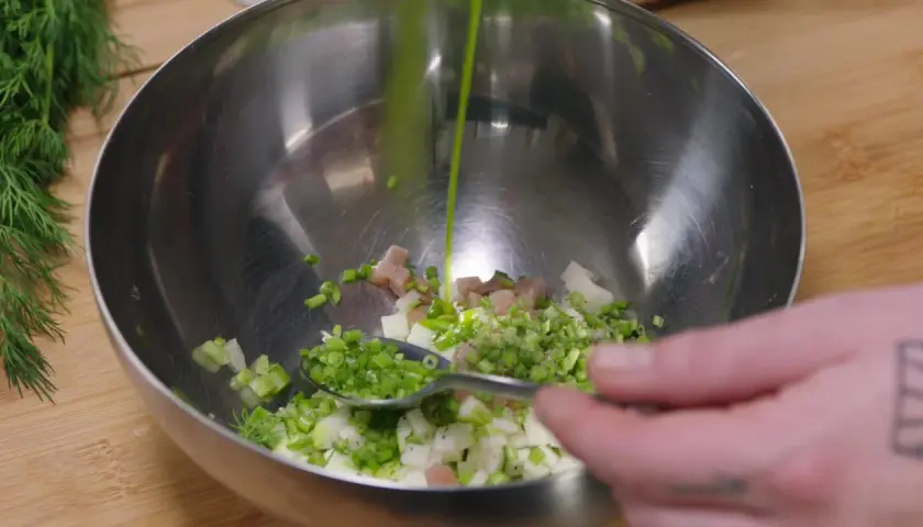 Préparation d'une salade nordique : on verse une sauce verte sur des dés de poisson, oignons et aneth dans un bol.