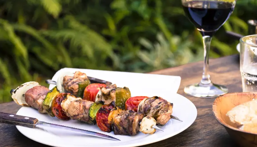 Brochettes de viande et légumes grillés, accompagnées d'un verre de vin pour grillade et d'un bol de pain.