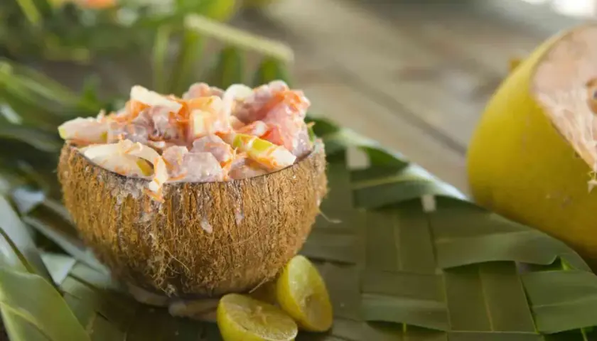 Salade tahitienne crémeuse servie dans une noix de coco, garnie de citron vert et de feuilles de palmier.