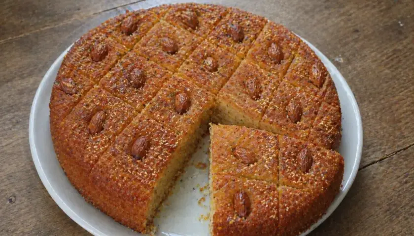 Un délicieux gâteau arabe au miel, parsemé d'amandes et de graines, coupé en carrés sur une assiette blanche.