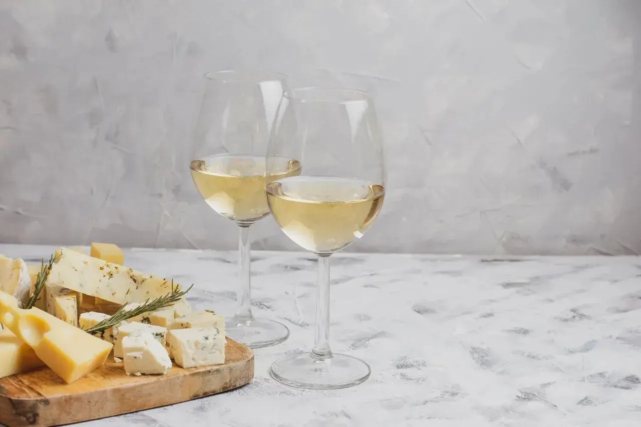 Deux verres de vin blanc pétillant, accompagnés d'une sélection de fromages sur une planche en bois.