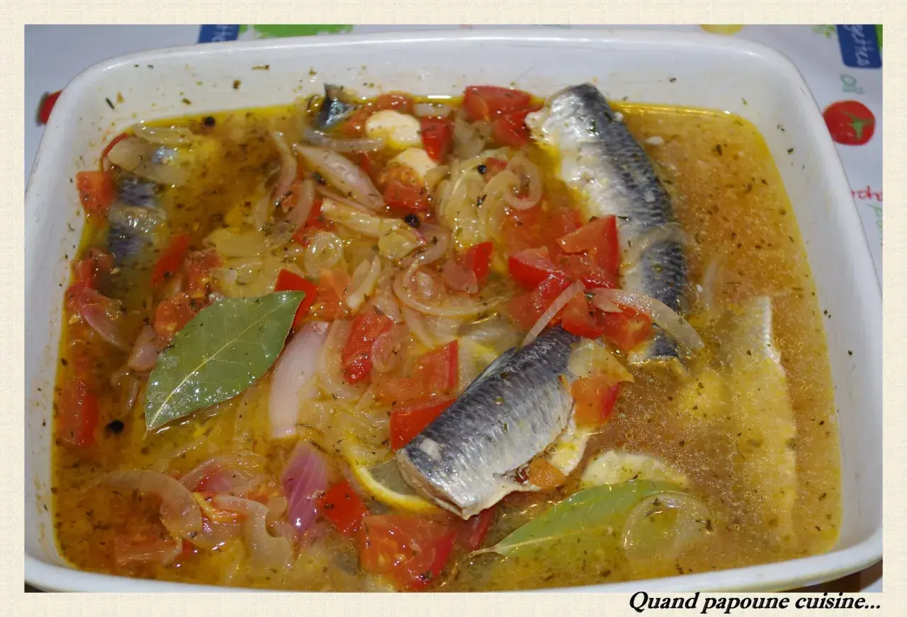 Sardines à l'escabèche dans un plat blanc, avec des tomates, oignons, citron et feuilles de laurier.