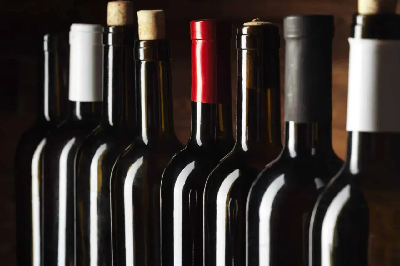Une rangée de bouteilles de vin rouge, certaines avec des capsules de différentes couleurs, pour vous aider à comment reconnaître un bon vin rouge.
