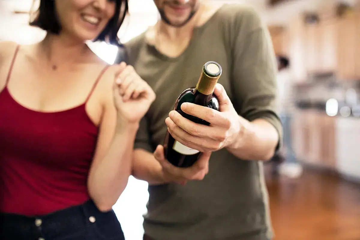 Un couple souriant admire une bouteille de vin rouge, prêt à partager un moment spécial.