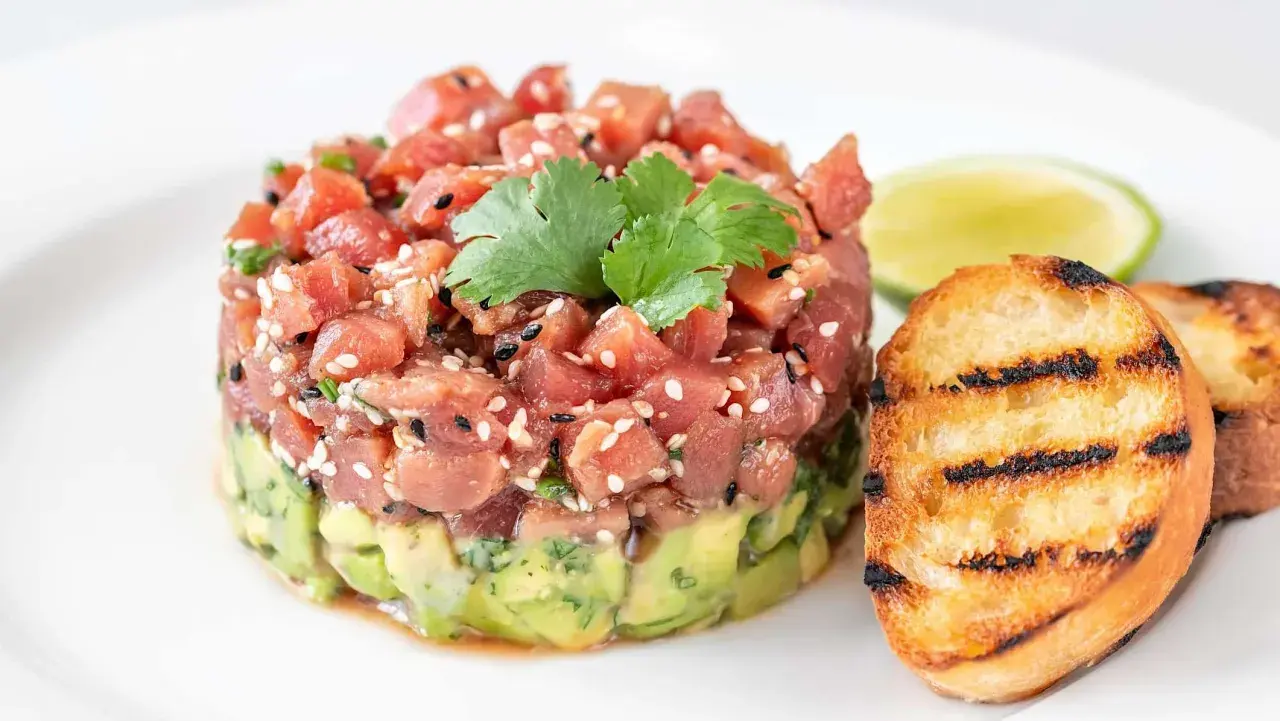 Délicieux tartare de bar frais, garni de sésame et de coriandre, servi avec des toasts grillés et une tranche de citron vert.