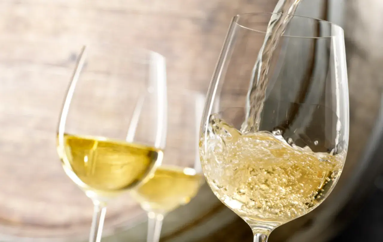 Le vin blanc est versé dans un verre, rappelant le processus de vinification. Deux autres verres sont visibles en arrière-plan.