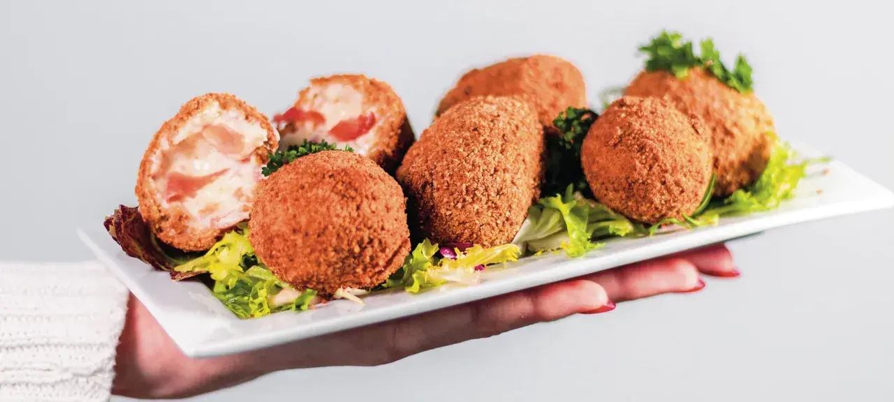 Assiette de croquetas de jambon dorées et croustillantes, garnie de salade verte.