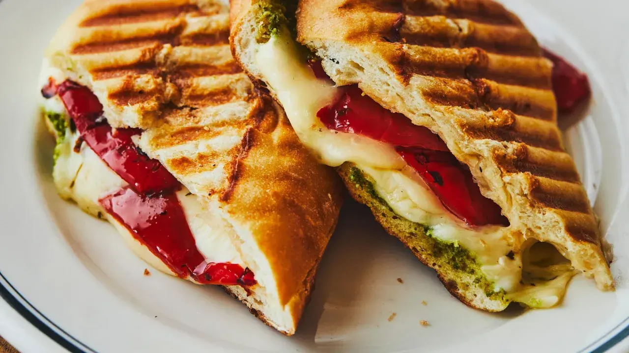 Un délicieux sandwich italien grillé, garni de fromage fondant, de poivrons rouges et de pesto vert.
