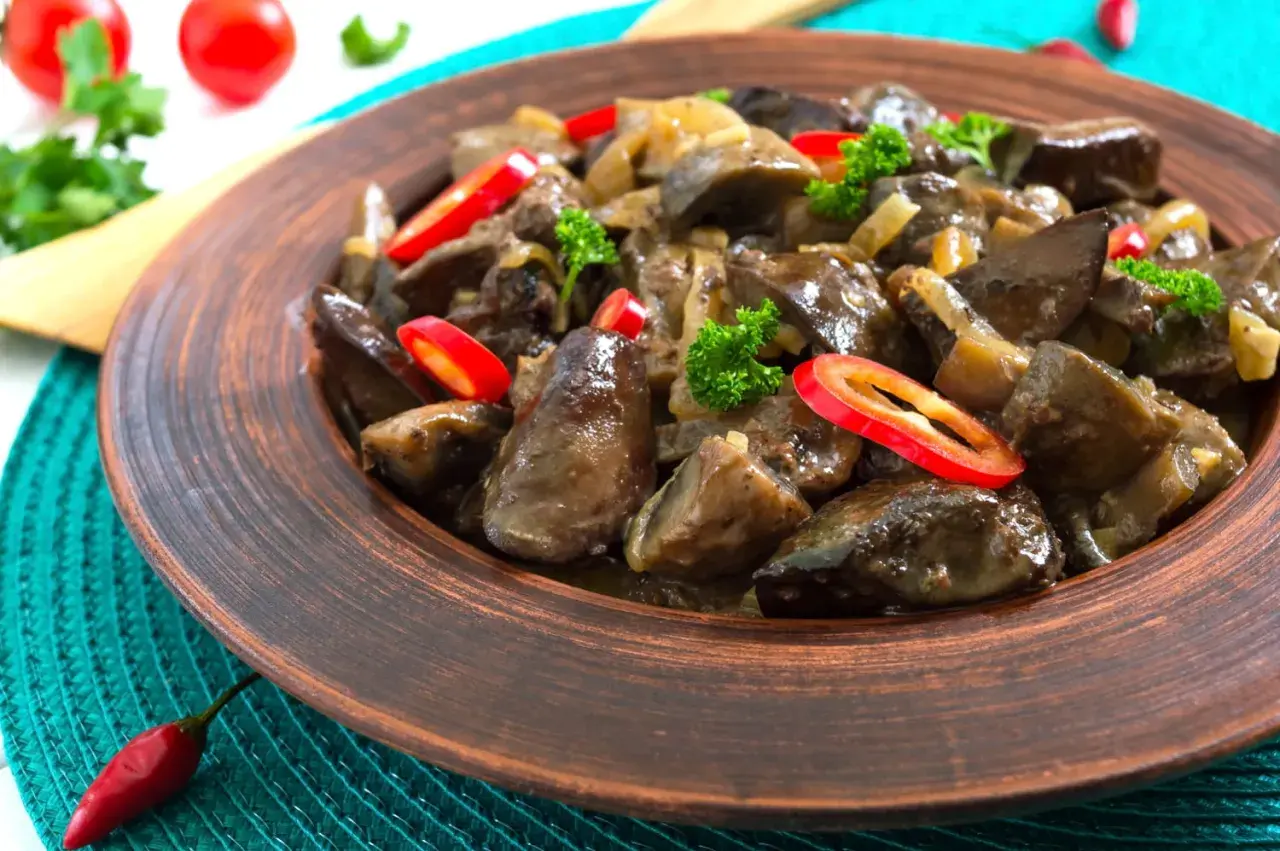 Un plat appétissant de foie de volaille mijoté avec des oignons et garni de persil frais et de rondelles de piment rouge.