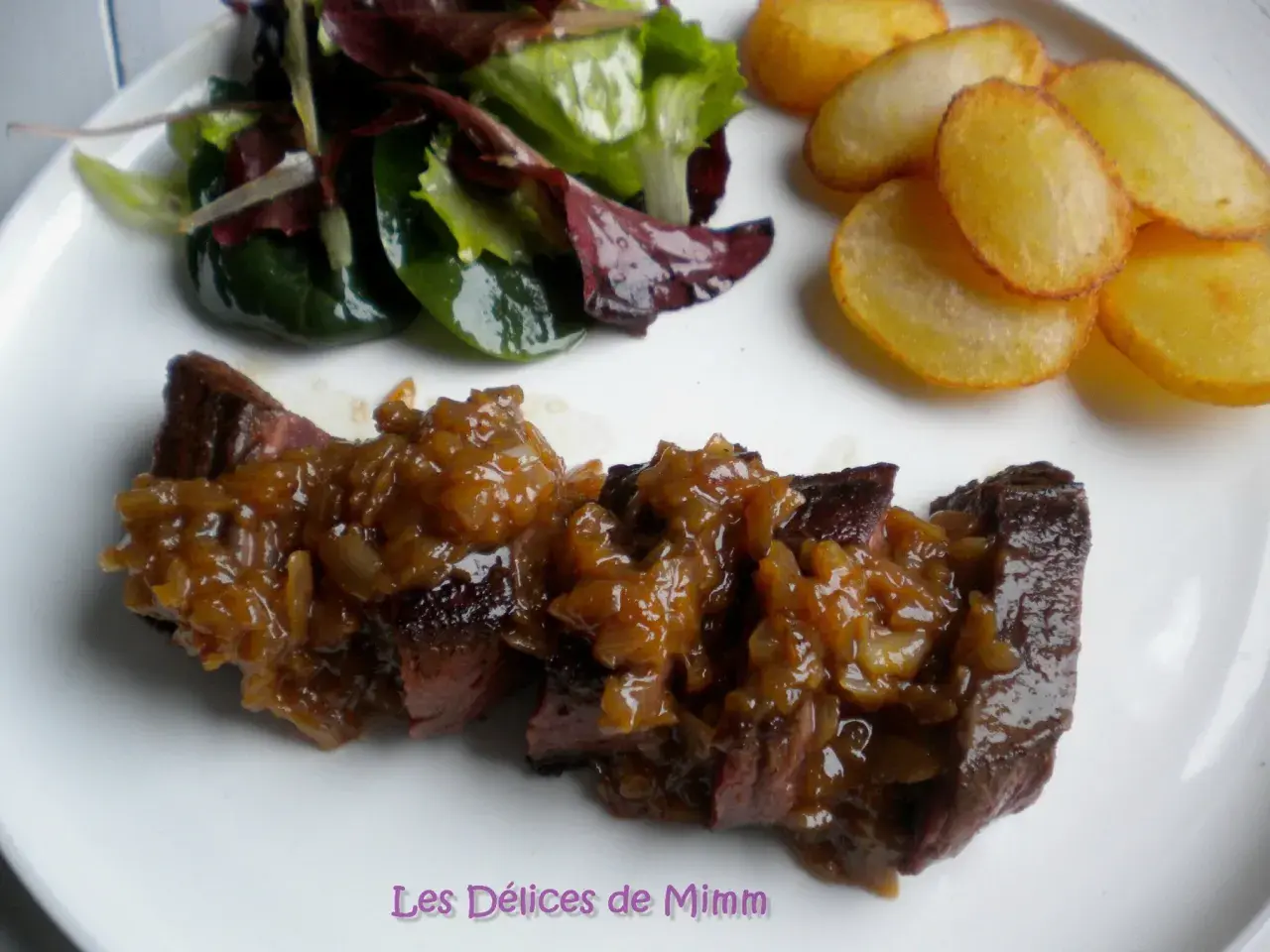 Un onglet à l'échalote, servi avec une salade verte et des pommes de terre sautées. Un plat savoureux et coloré.