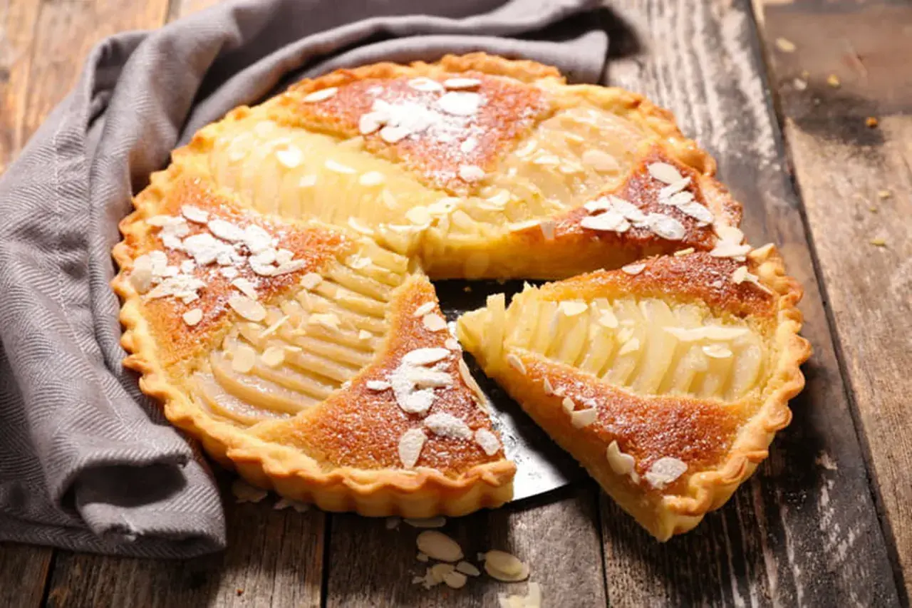 Une délicieuse tarte au poire, garnie d'amandes effilées et saupoudrée de sucre glace, repose sur un plateau en bois.