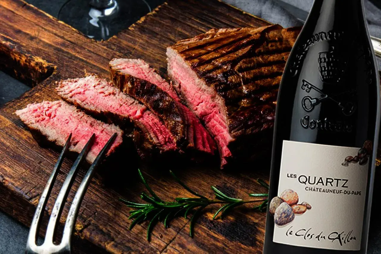 Un steak grillé et tranché sur une planche en bois, accompagné d'une bouteille de vin rouge passe partout.