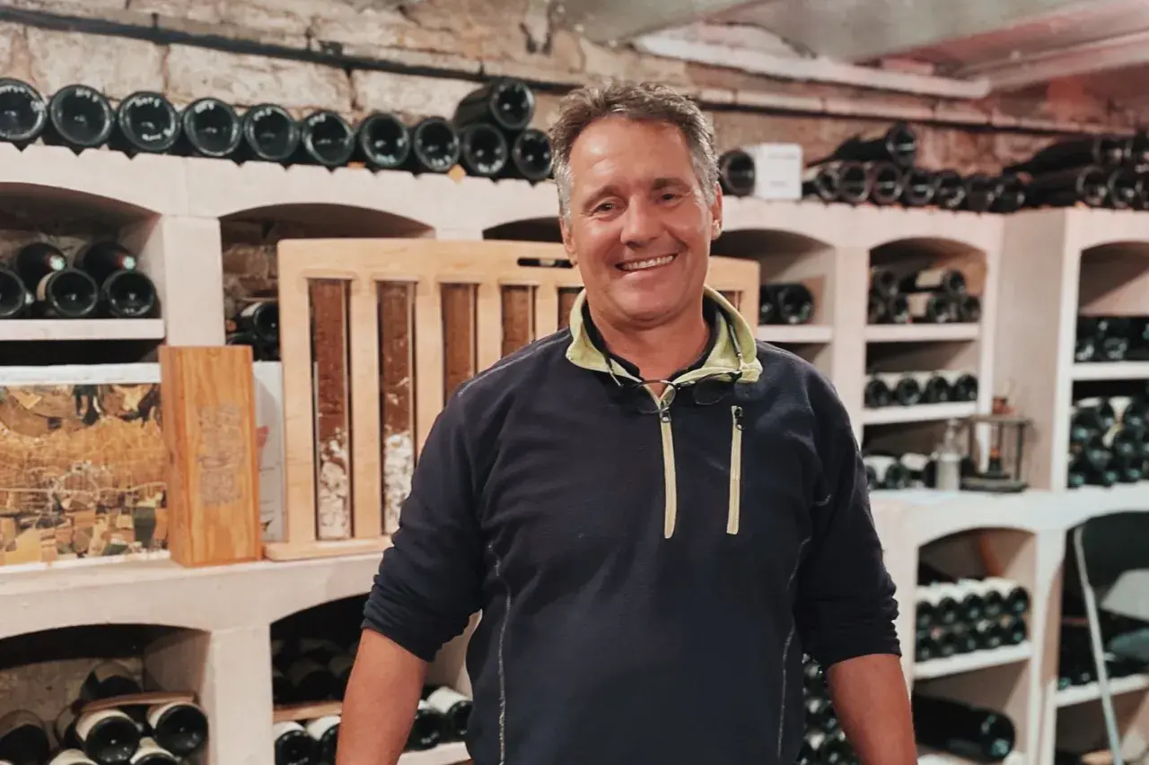 Bruno Clavelier, vigneron souriant, pose dans sa cave remplie de bouteilles.