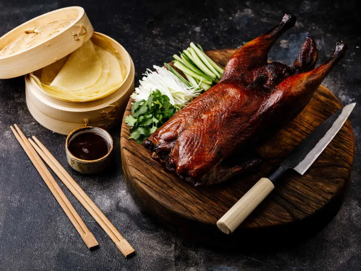 Un canard laqué prêt à être dégusté, accompagné de ses crêpes, sauce, légumes croquants et coriandre. Une recette parfaite pour un repas festif.