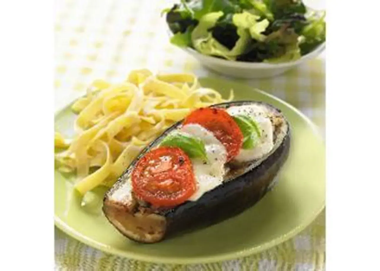 Aubergine farcie de mozzarella, tomates et basilic, servie avec des pâtes et une salade verte. Un plat savoureux et coloré.