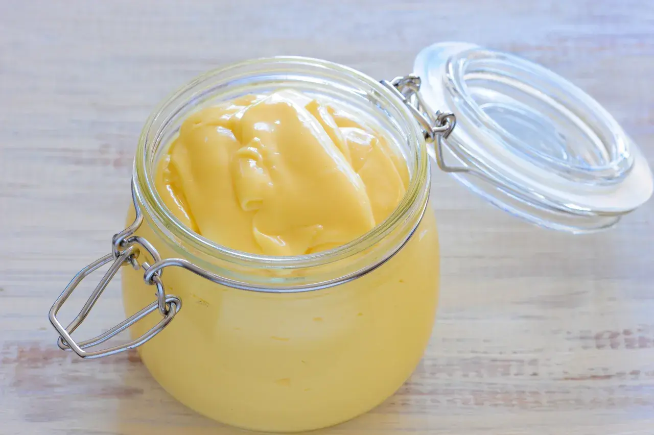 Un pot en verre ouvert révèle une mayonnaise onctueuse, faite maison avec de la mayonnaise huile d'olive.