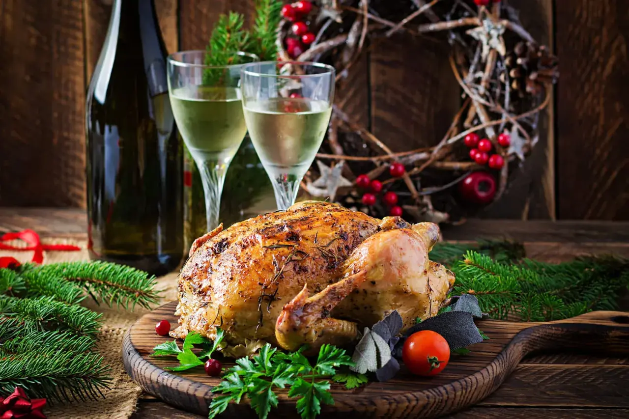 Un chapon rôti, prêt à être dégusté, avec deux verres de vin blanc et une décoration festive. Quel vin avec du chapon pour ce repas de fête ?