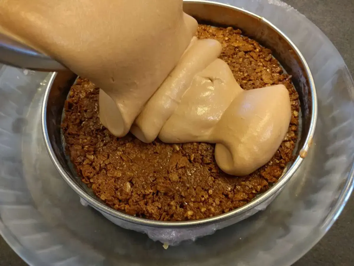 Une crème onctueuse est versée sur une base croustillante praliné feuilletine dans un cercle à pâtisserie.