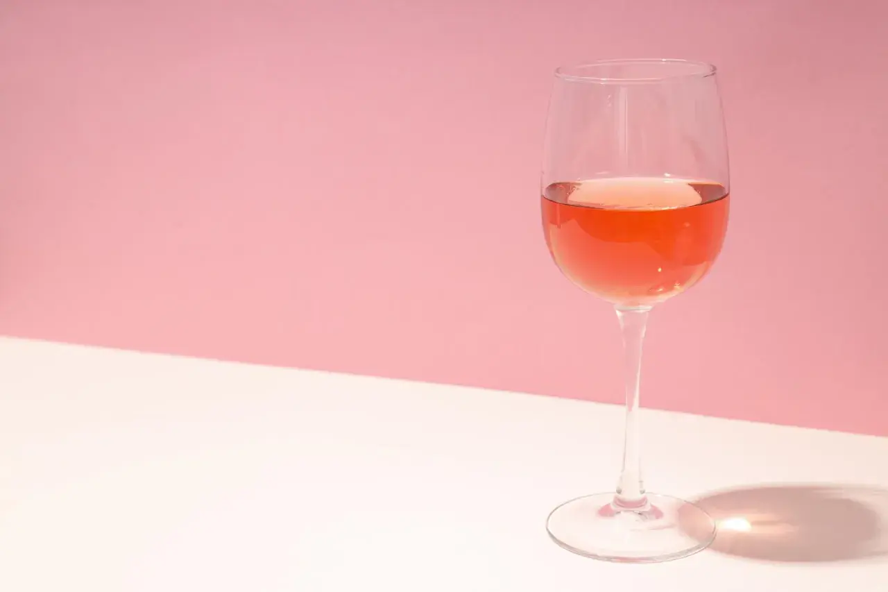 Un verre de rosé de macération, d'une belle couleur orangée, sur un fond rose et blanc.