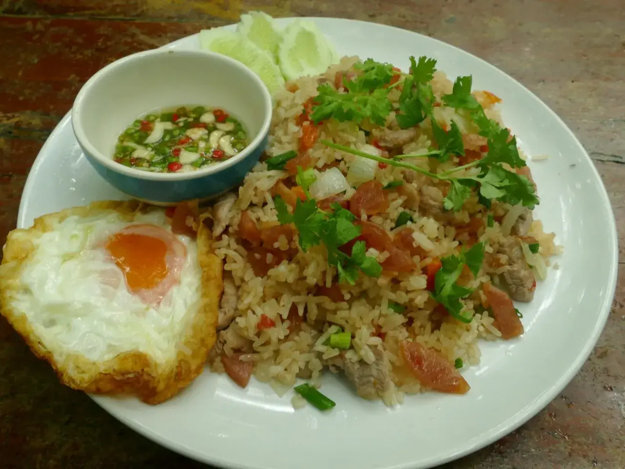 Un plat de riz thaï savoureux avec un œuf au plat, des tranches de concombre et une sauce piquante.